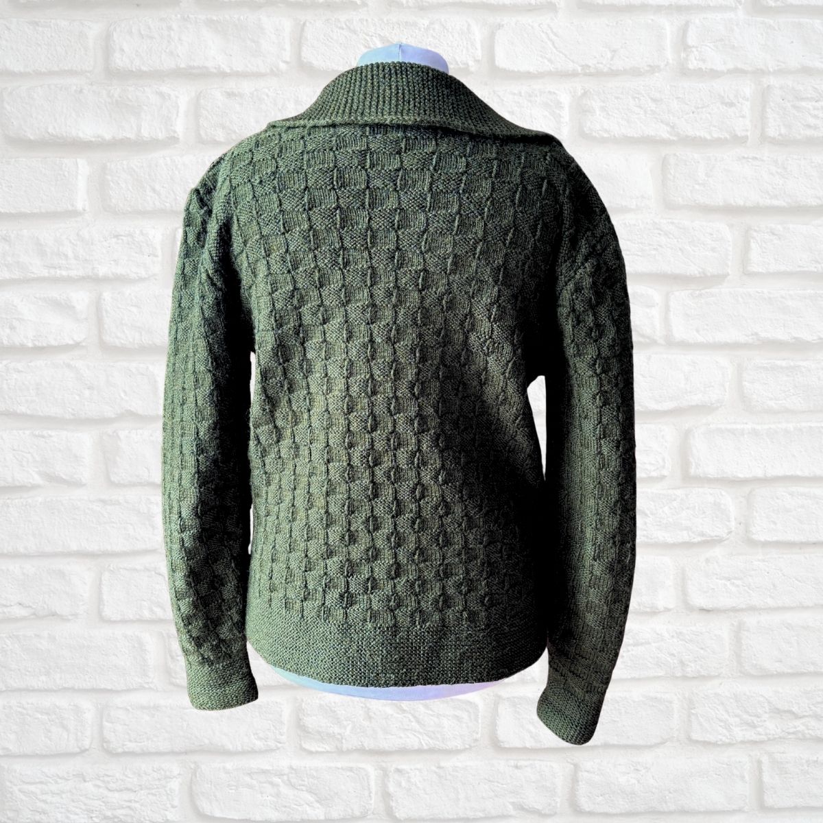 An olive green textured knit sweater displayed on a mannequin torso against a white brick wall background.