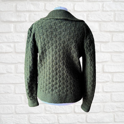 An olive green textured knit sweater displayed on a mannequin torso against a white brick wall background.