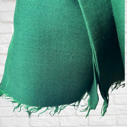 A vibrant green woven scarf with frayed edges draped against a white brick wall background.