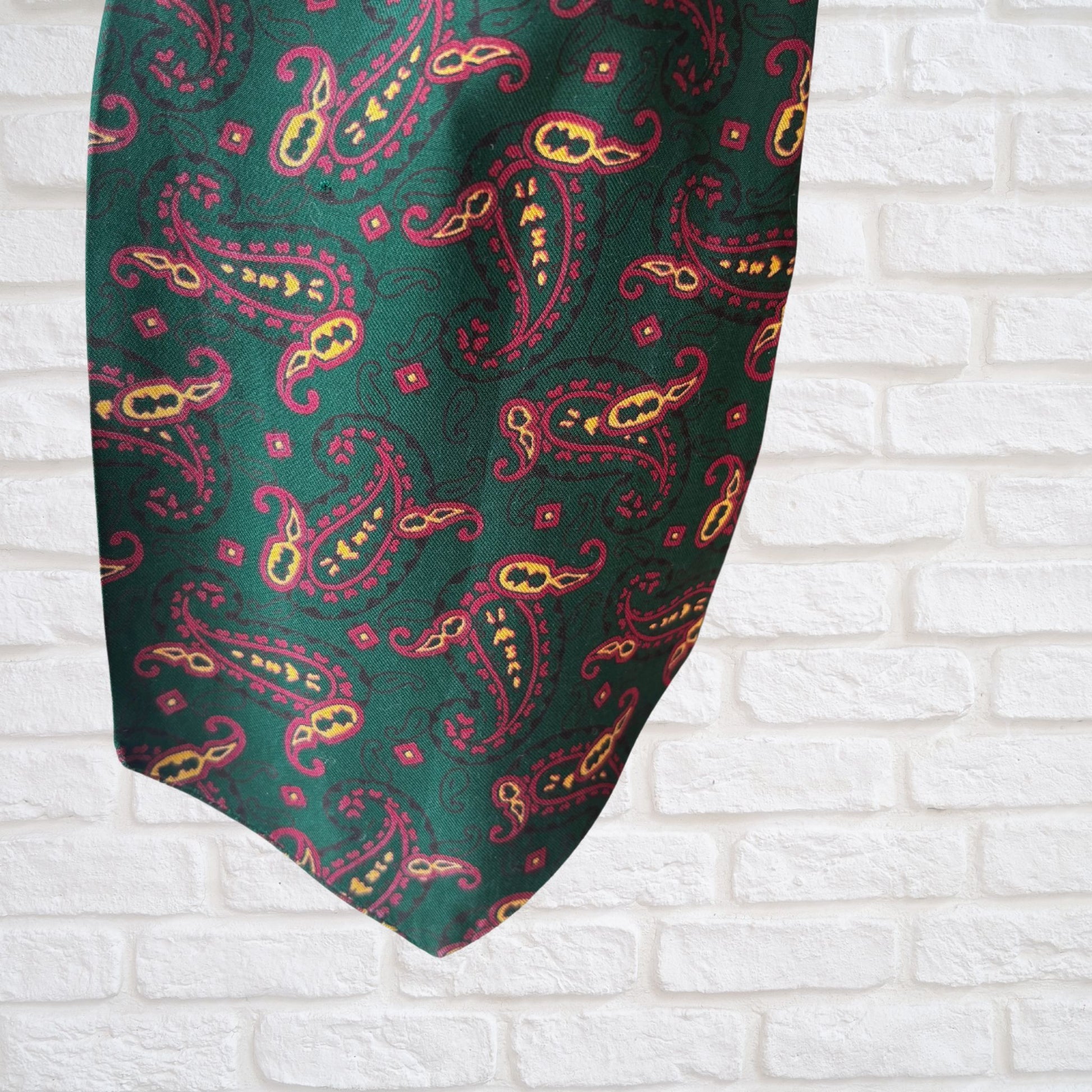 Green paisley patterned tie against a white brick wall background