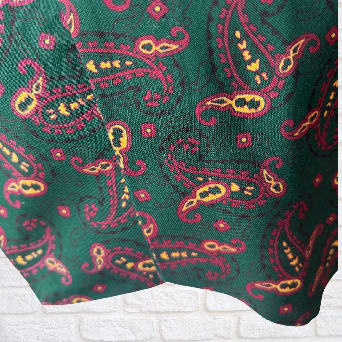 Close-up of a green fabric with red and yellow paisley pattern on a white background