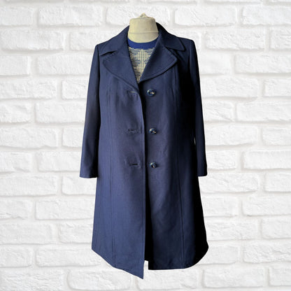 A navy blue mid-length coat displayed on a dress form mannequin against a white painted brick wall background.