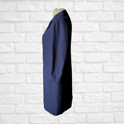A navy blue long-sleeve coat or jacket displayed on a mannequin torso against a white painted brick wall background.