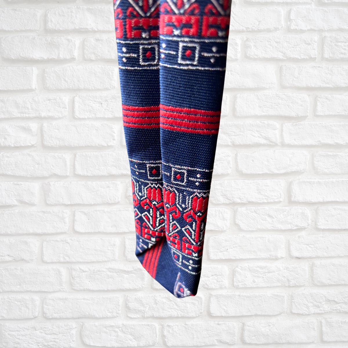 Blue and red patterned tie against a white brick wall background