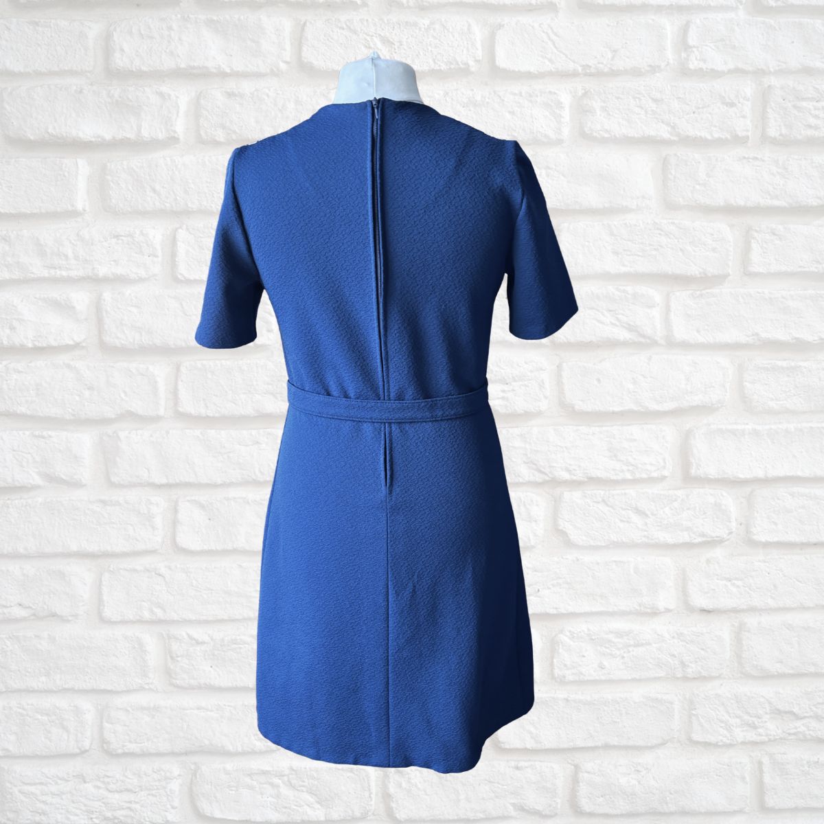 Blue mini dress on a mannequin against a white brick wall background