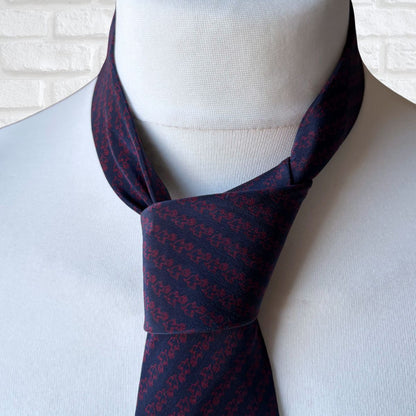 Navy blue necktie with red pattern on a mannequin against a white brick wall.