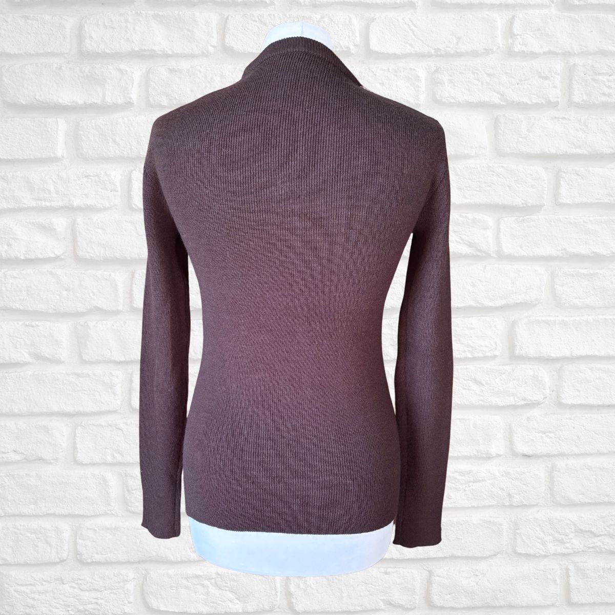 A dark brown  ribbed knit long-sleeve top displayed on a mannequin torso against a white brick wall background.