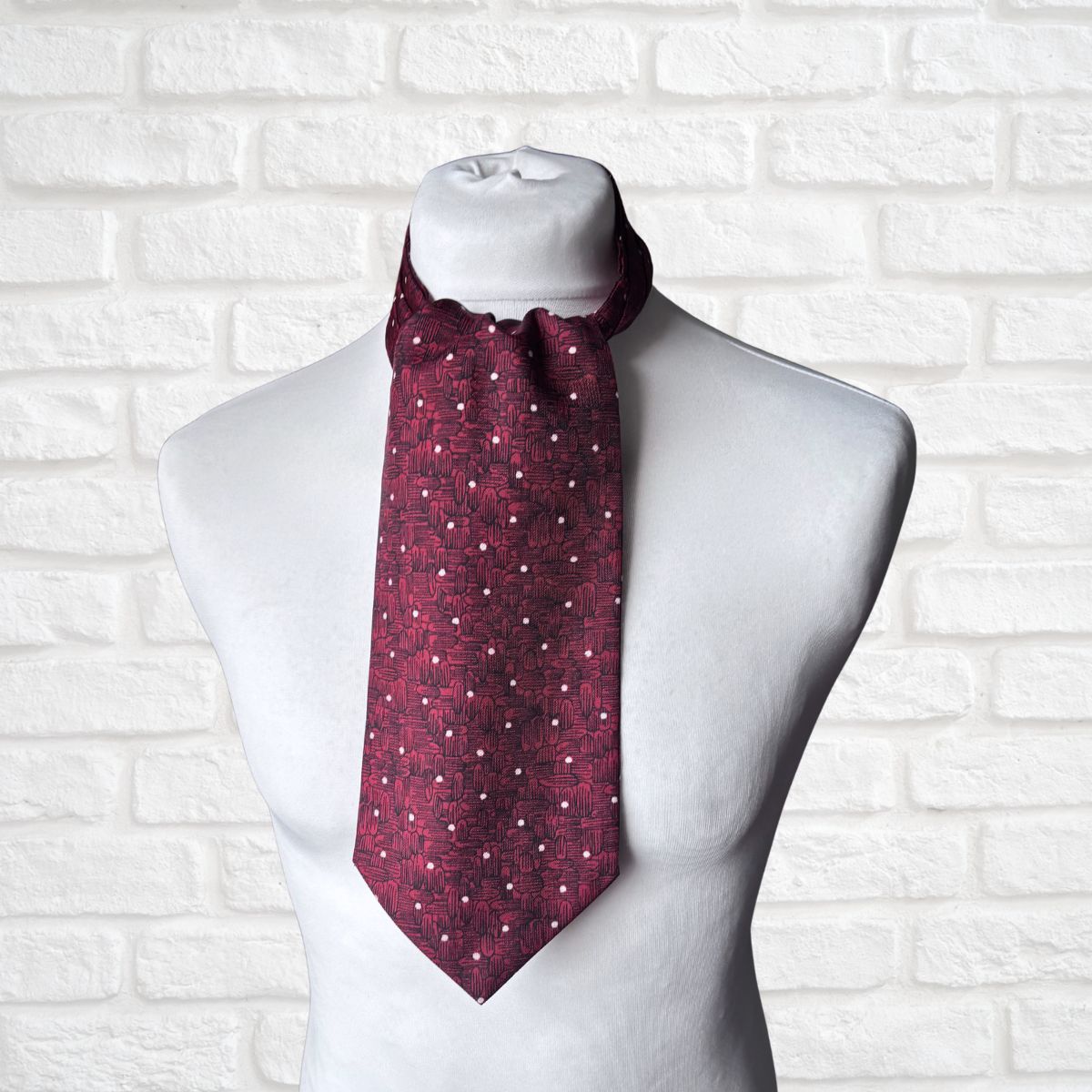 Maroon patterned cravat  on a mannequin against a white brick wall background