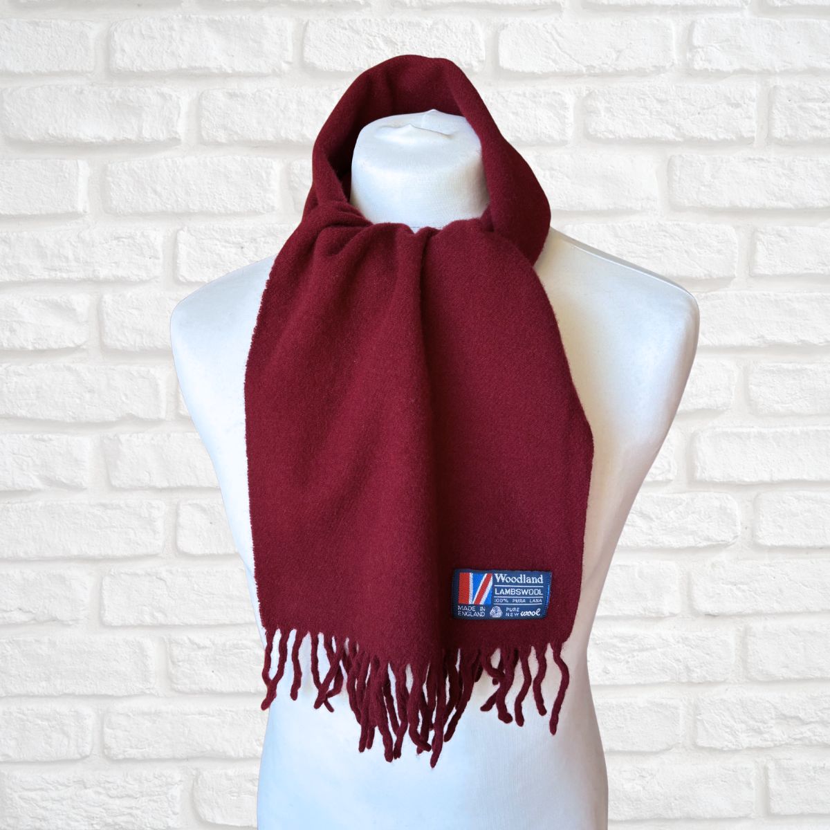 Red scarf with a brand label on a mannequin against a white brick wall.