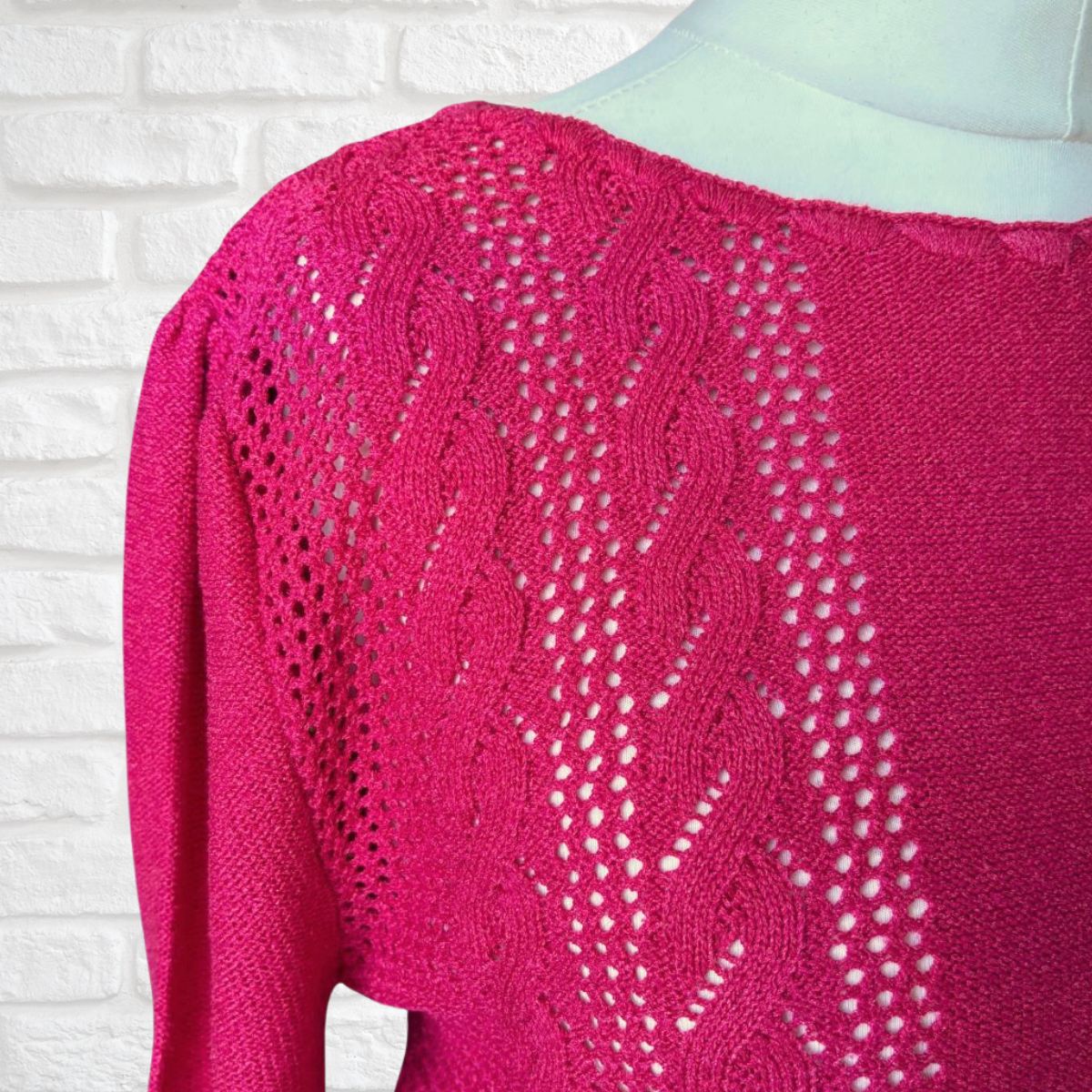 Pink knitted sweater with intricate pattern on a white brick wall background