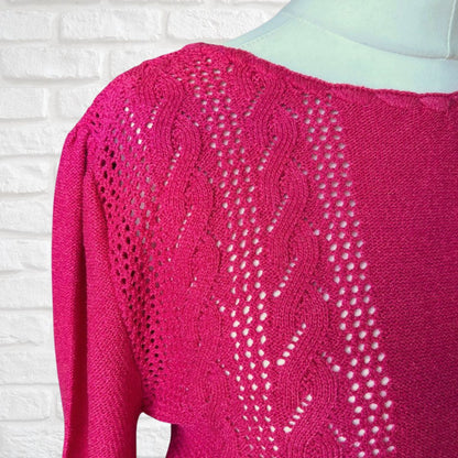 Pink knitted sweater with intricate pattern on a white brick wall background