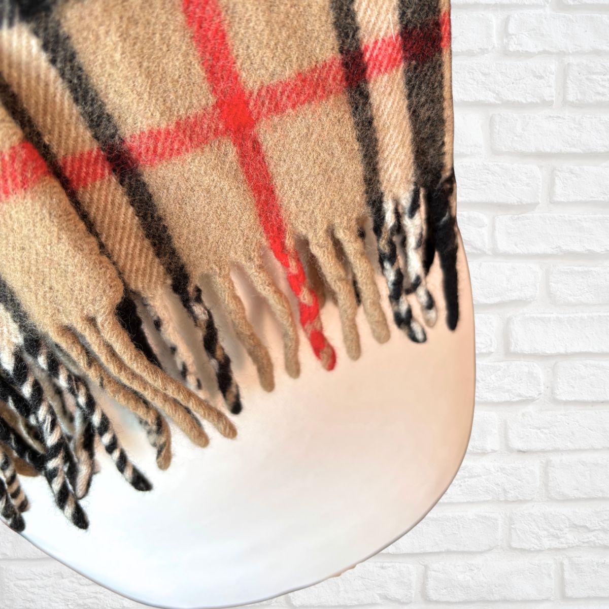 Plaid scarf with beige, red, and black colors on a white brick wall background