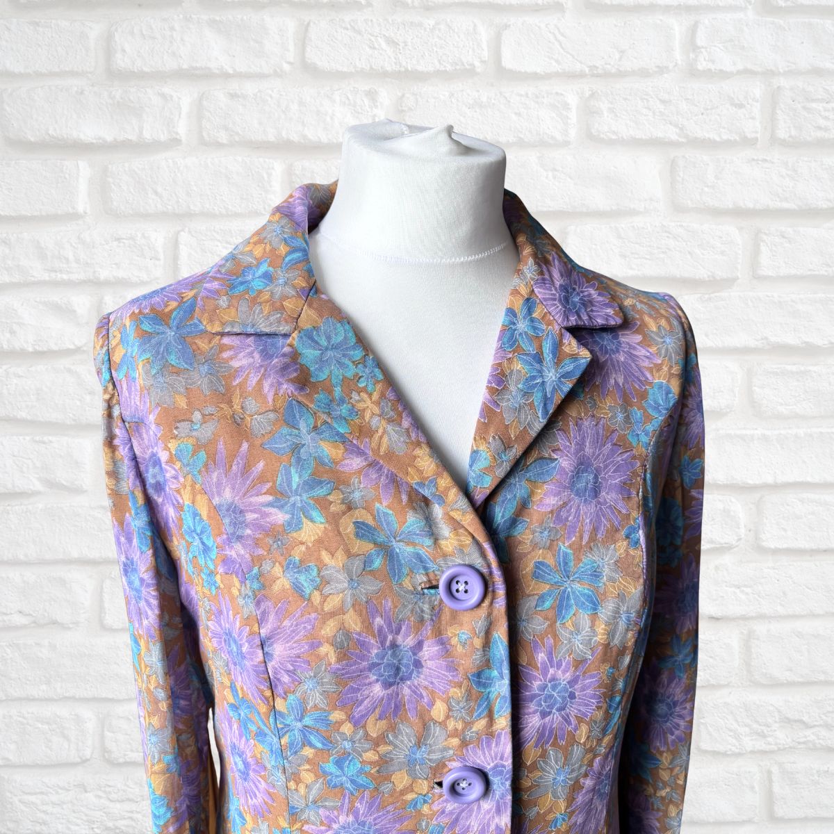 Floral patterned dress  on a mannequin against a white brick wall.