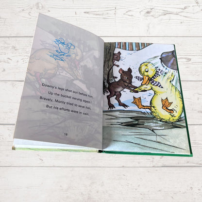 An open children's book lying on a white wood surface, showing illustrated pages with a yellow duck, a brown animal, and printed text.