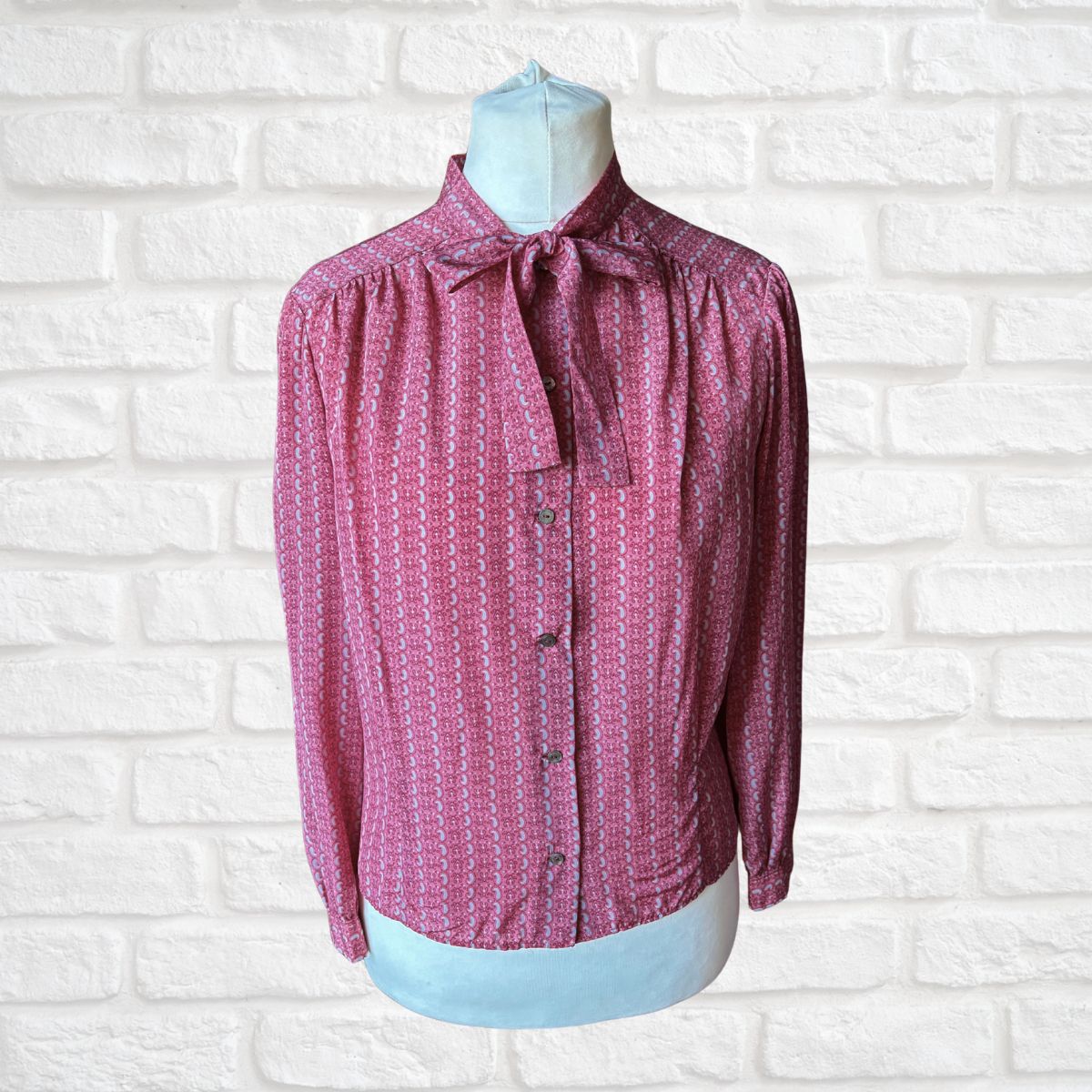 Pink patterned blouse on a mannequin against a white brick wall background