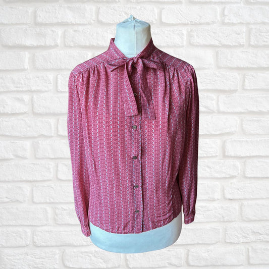 Pink patterned blouse on a mannequin against a white brick wall background