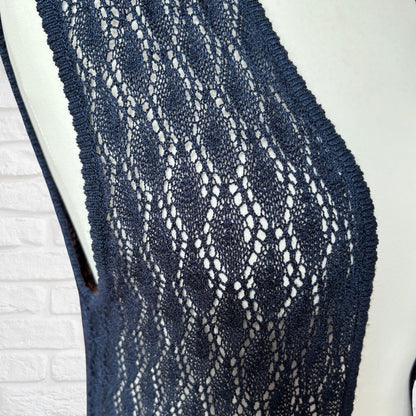 A close-up of a navy blue open-knit lace top or vest displayed on a white mannequin torso against a white brick wall background.