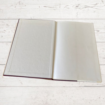 An open blank book with cream-colored pages, displayed flat on a light whitewashed wooden surface.