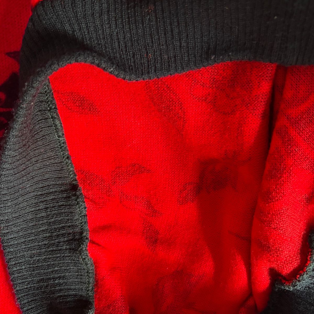 Close-up of a red garment with a black ribbed knit trim and a subtle tonal floral pattern on the red fabric.