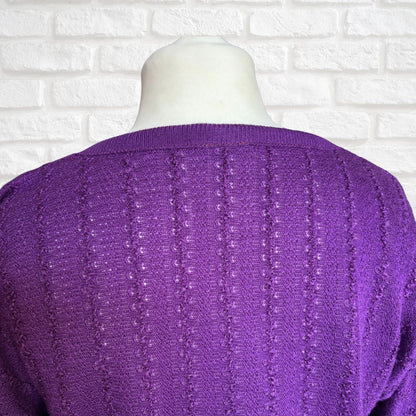 A close-up of a purple knit sweater with vertical textured stripes, displayed on a white mannequin torso against a white brick wall background.