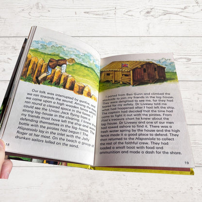 An open printed book spread showing two pages with text and a small inset photograph of a ship on the right page, held in a person's hand against a light wood background.