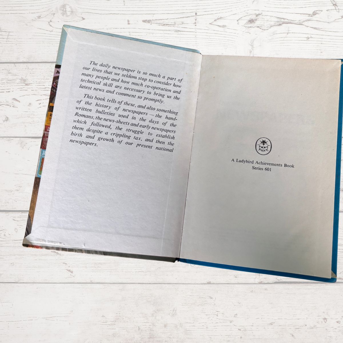 An open book titled 'The Daily Newspaper' displayed on a white wooden surface. The left page contains text, and the right page shows the title 'A Ladybird Achievement Book Series 601' along with a Ladybird logo.