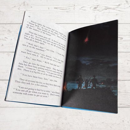 Open book with text on one page and a dark scene with people on the other, on a light wooden surface.