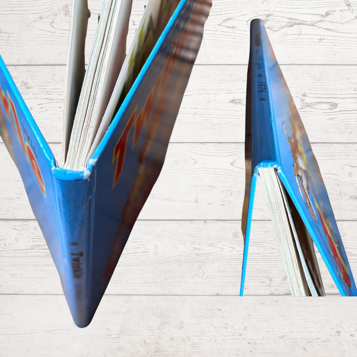 A close-up of a hardcover book with a bright blue spine and colorful cover pages, shown partially open on a light wood plank surface.