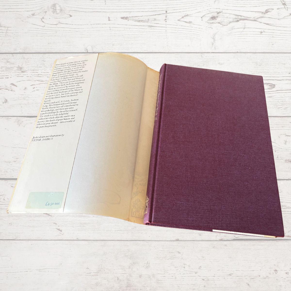 An open vintage hardcover book with cream-colored pages and a textured dark purple-brown cloth binding, displayed on a white wood plank background.