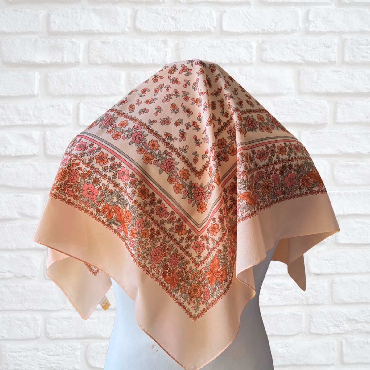 Peach scarf with floral pattern draped over a mannequin against a white brick wall.