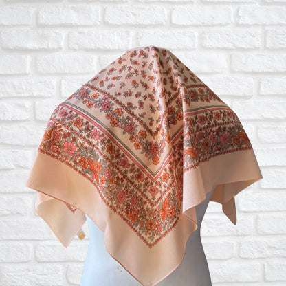 Peach scarf with floral pattern draped over a mannequin against a white brick wall.