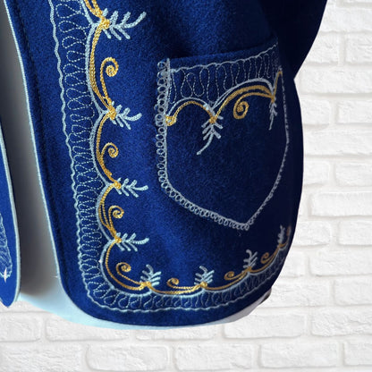 Blue waistcoat  with intricate white and gold embroidery on a white brick wall background