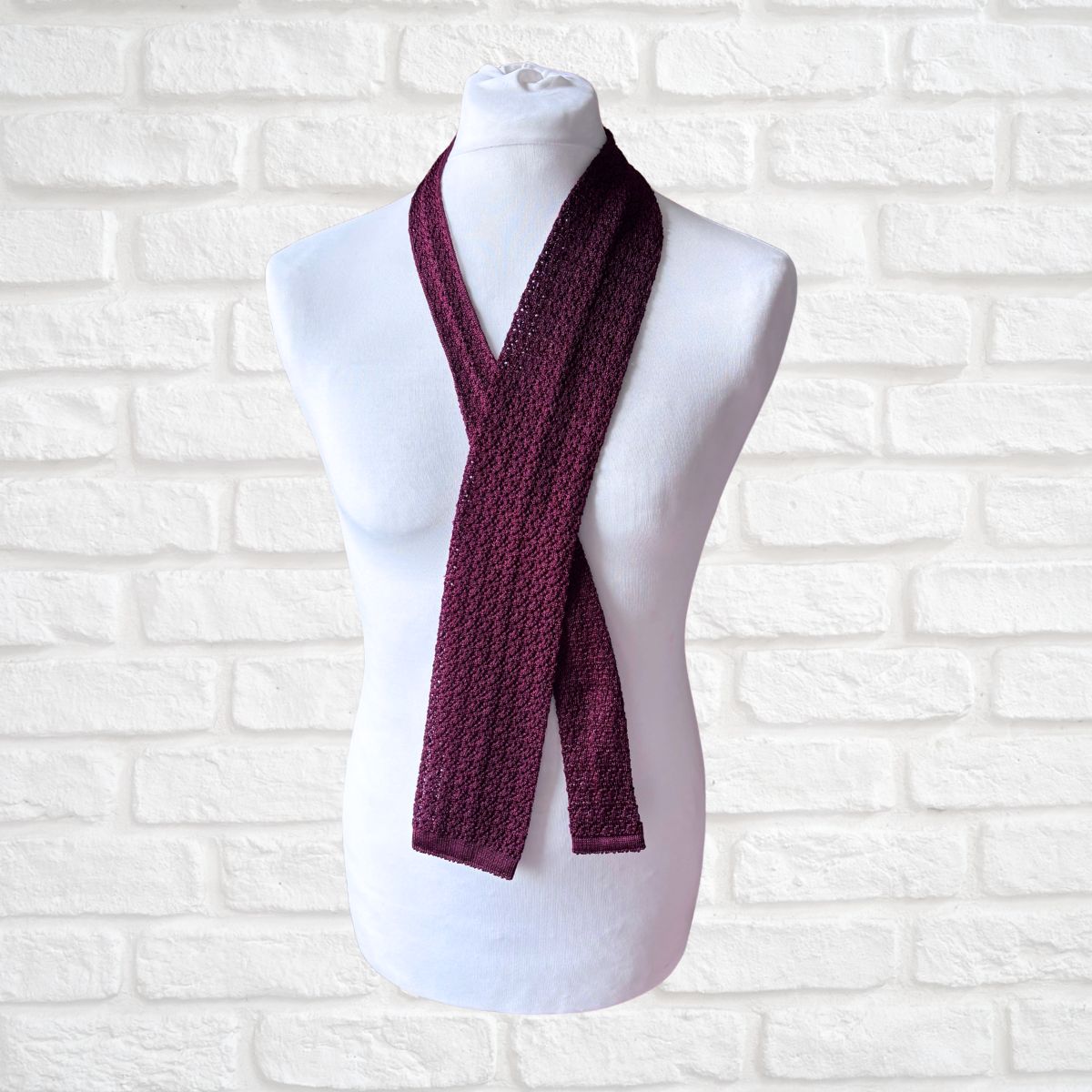 Maroon knitted scarf on a mannequin against a white brick wall background