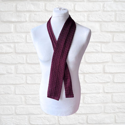 Maroon knitted scarf on a mannequin against a white brick wall background