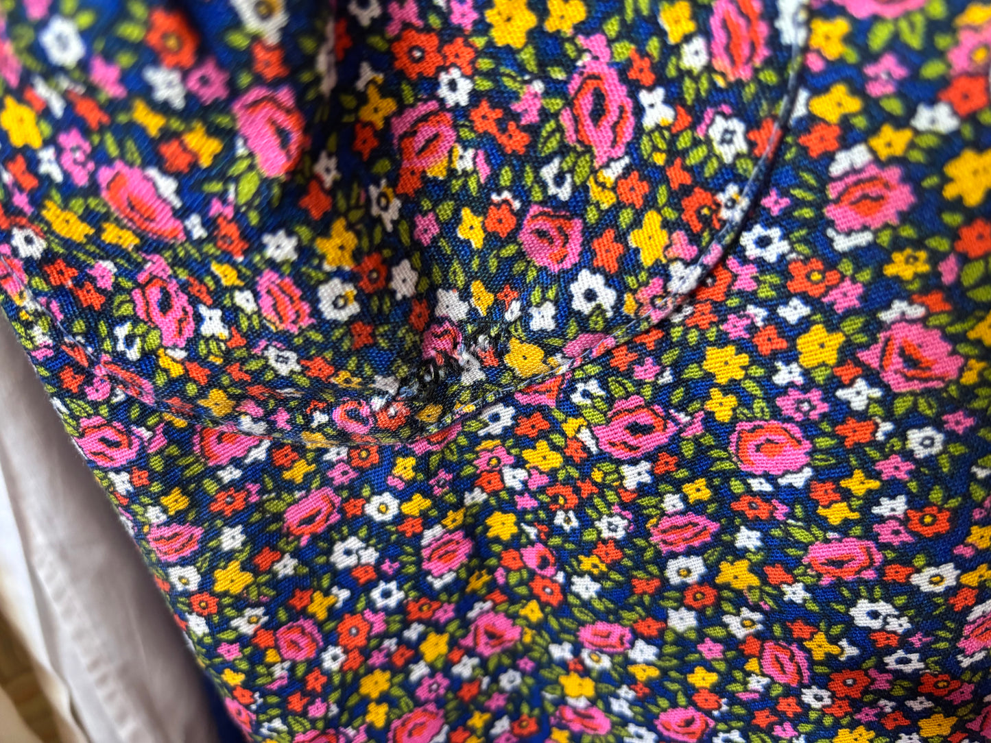 Close-up of a dark navy blue fabric with a dense, colorful floral pattern featuring pink, yellow, orange, and white flowers with green leaves.