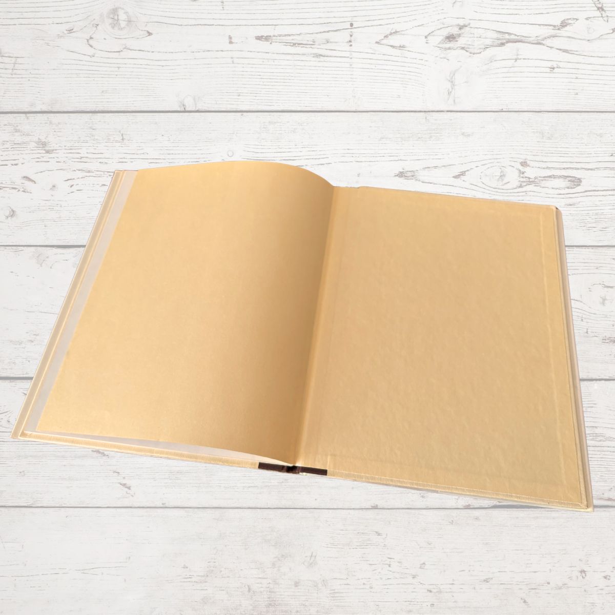 An open blank book with tan pages, displayed flat on a white-washed wooden plank surface.