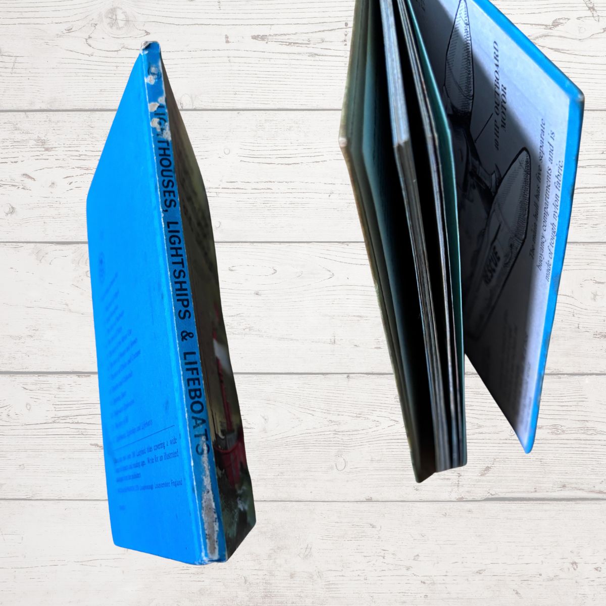 A hardcover book titled 'Houses, Lightships & Lifeboats' shown standing upright and partially open, with a bright blue spine and matching blue cover edge, photographed against a light wood plank background.