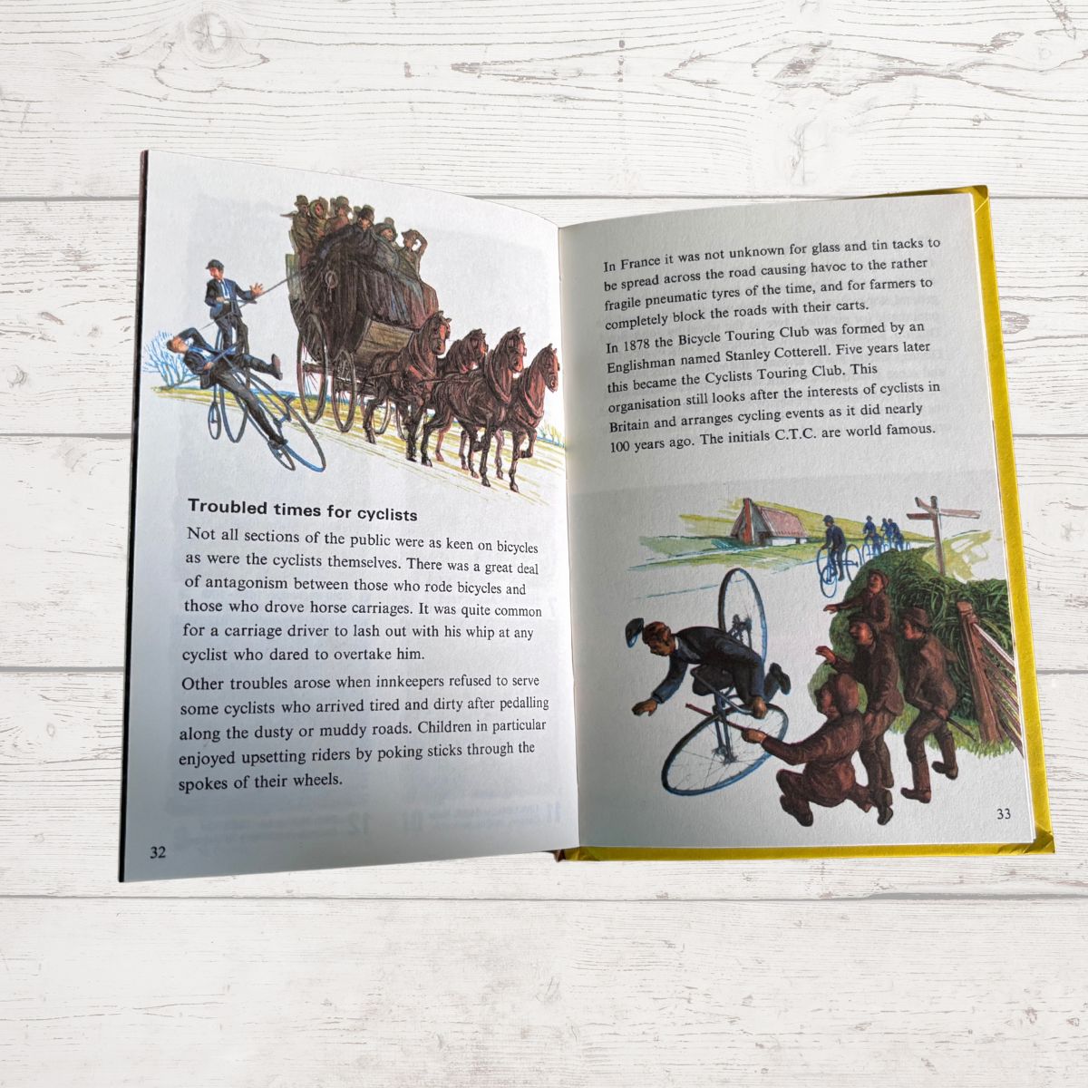 An open vintage children's book spread showing illustrated pages about cycling, photographed on a white painted wood surface.