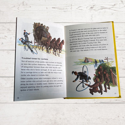 An open vintage children's book spread showing illustrated pages about cycling, photographed on a white painted wood surface.