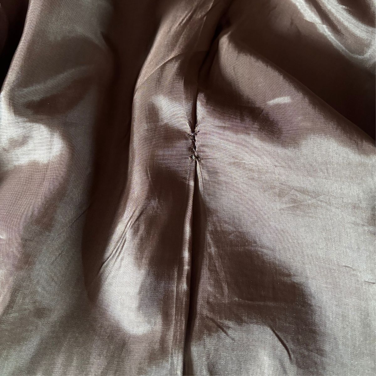 A close-up of a brown satin or silk-like fabric with a central seam and soft folds, showing a subtle sheen