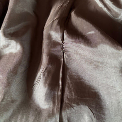 A close-up of a brown satin or silk-like fabric with a central seam and soft folds, showing a subtle sheen