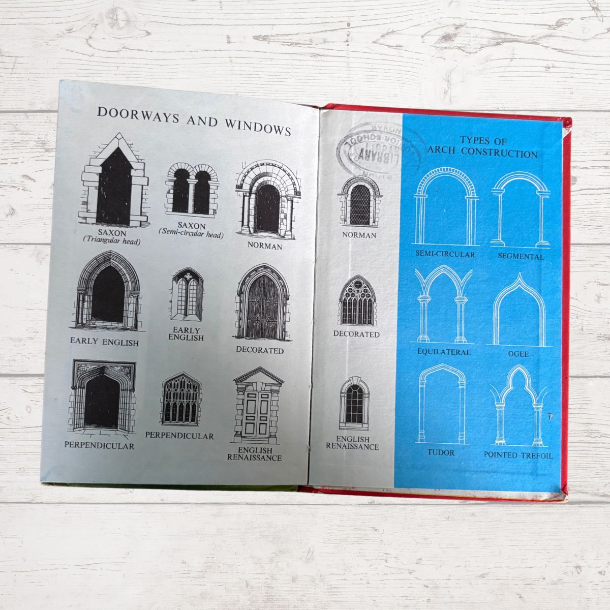 An open book showing architectural diagrams of doorways and windows, with black line drawings on a light gray page and blue line drawings on a blue page, photographed on a white wood surface.