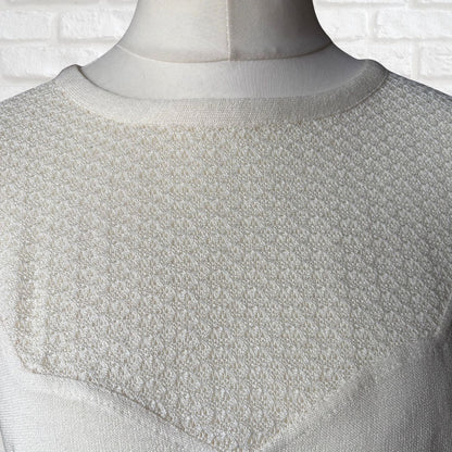 Textured white garment on a mannequin against a white brick wall.