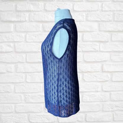 A sleeveless blue crochet  knit vest displayed on a light blue mannequin torso, set against a white brick wall background.