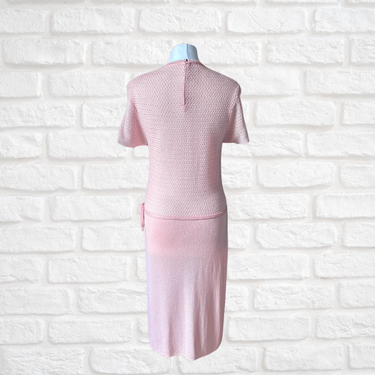 A light pink knitted pencil dress  displayed on a mannequin against a white brick wall background