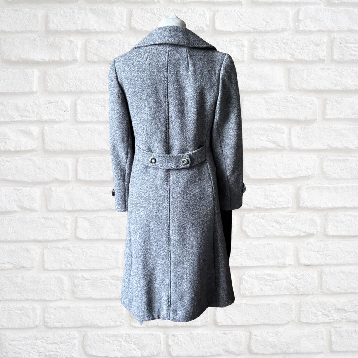 Grey coat on a mannequin against a white brick wall background