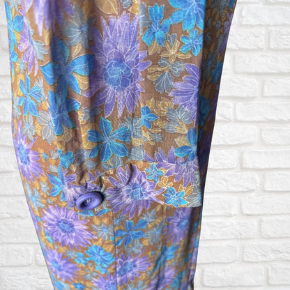 Floral-patterned dress with purple and blue flowers on a brown background against a white brick wall.