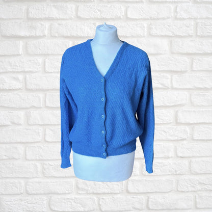 A bright blue textured knit cardigan sweater displayed on a light blue mannequin torso against a white faux-brick background.