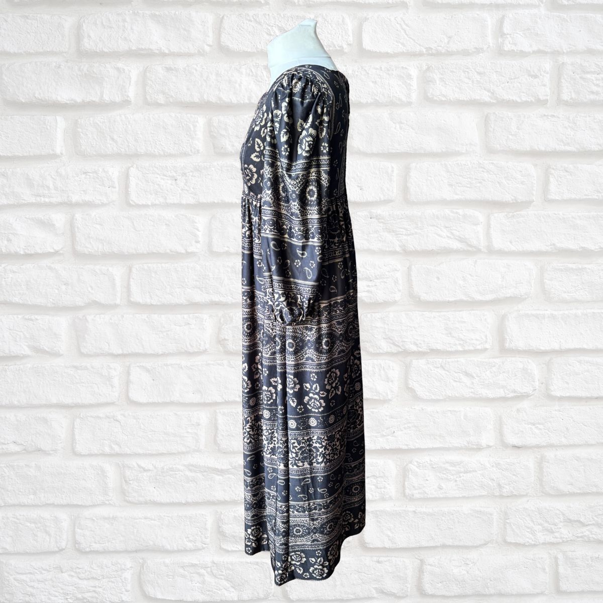 Black and white patterned dress on a mannequin against a white brick wall background