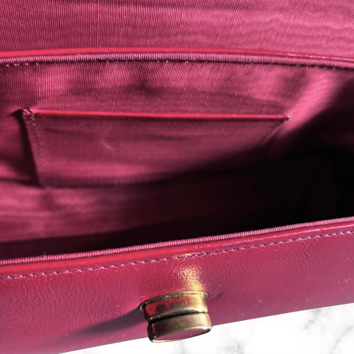Close-up of the interior of a red  leather handbag, showing a satin-lined pocket and a gold-tone metal snap closure.